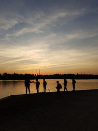 Silhouette people on beach against sky during sunset