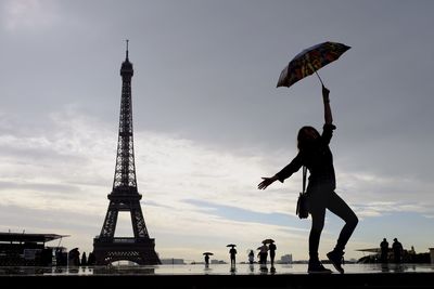Woman holding umbrella while standing against eiffel tower during sunset