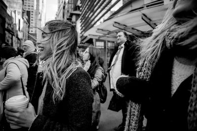 Happy young woman holding drink while walking on city street