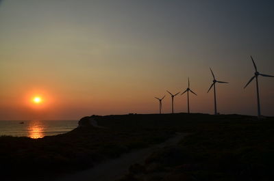 Silhouette wind turbines against sky during sunset