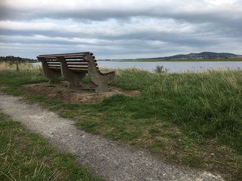 Bench on field by lake against sky