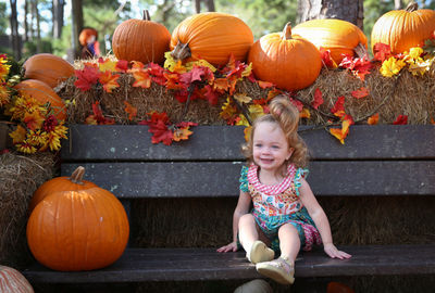 Full length portrait of smiling girl with pumpkin in park during autumn