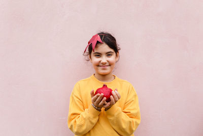 Smiling girl holding red pomegranate againts pink wall