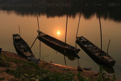 Boat moored at lakeshore against sky during sunset