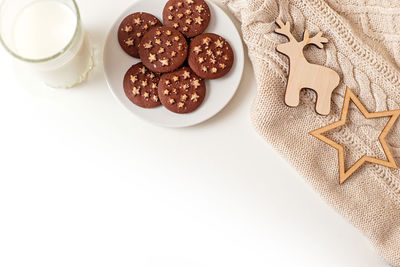 On a white table a saucer with round chocolate chip cookies, a glass of milk