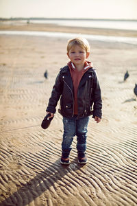 Child boy in a hoodie holds a leash with a dog in autumn standing on the sand