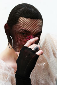 Close-up of man covering face while wearing fishnet stockings over white background