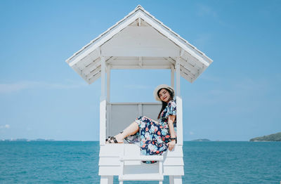 Woman sitting by sea against sky