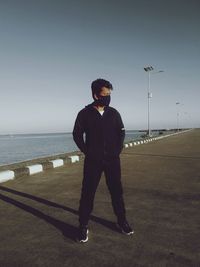 Full length of man wearing mask standing on road against clear sky