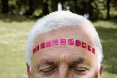 Cropped image of senior man with decorations on forehead at park