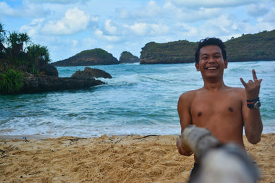 Portrait of shirtless man at beach against sky