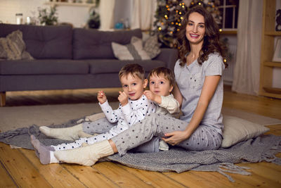 Mom hugs her two sons sitting on the floor of the house next to the christmas tree