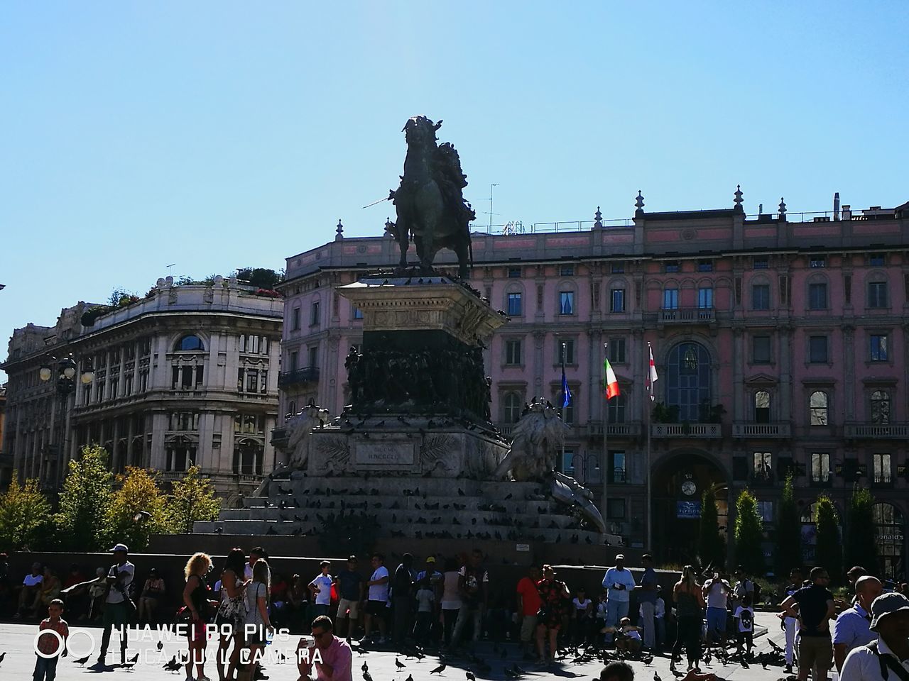 statue, architecture, sculpture, built structure, building exterior, human representation, art and craft, art, horse, large group of people, window, clear sky, monument, city, creativity, blue, town square, history, travel destinations, old town, day, city life, culture, outdoors, pedestal, crowd, sky