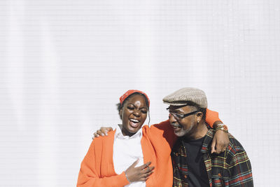 Daughter and father laughing while standing against wall on sunny day