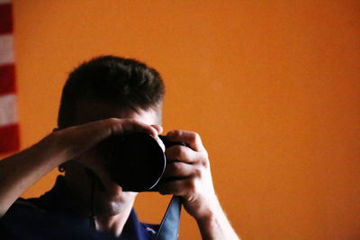 Close-up of man photographing with camera against orange wall