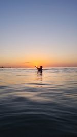 Silhouette person in sea against sky during sunset