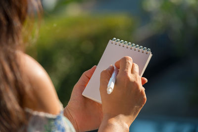 Midsection of woman writing in paper outdoors