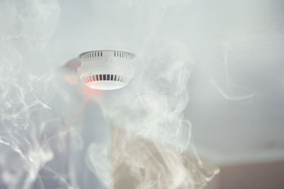 Low angle view of smoke by fire alarm on ceiling