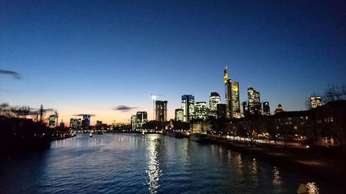 Illuminated city by river against sky at night