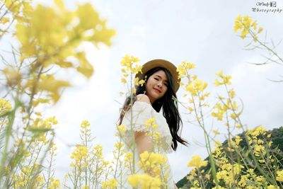 Portrait of beautiful young woman standing by yellow flower in field