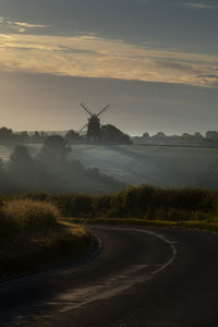 Road amidst field against sky during sunset