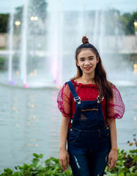 Portrait of smiling young woman standing against fountain