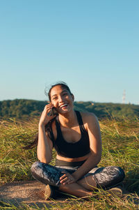 Young woman sitting on field against clear sky