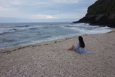 Woman sitting on rock by sea against sky