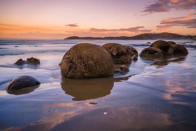 Rocks on beach against sky during sunset