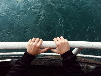 Cropped hand of woman holding railing of nautical vessel on sea