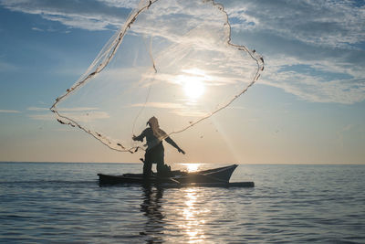 Man fishing in sea against sky during sunset