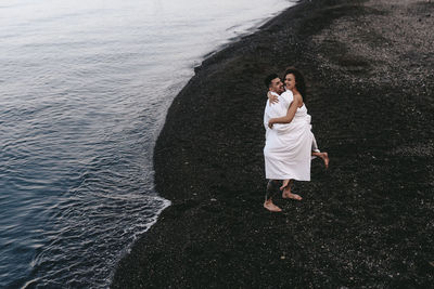 A diverse of lovers a man and a woman embrace under a blanket on the ocean at night outdoor