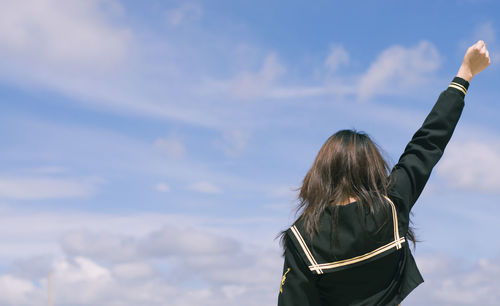 Rear view of woman with hand raised standing against sky