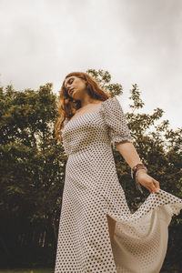 Portrait of woman standing by tree against sky