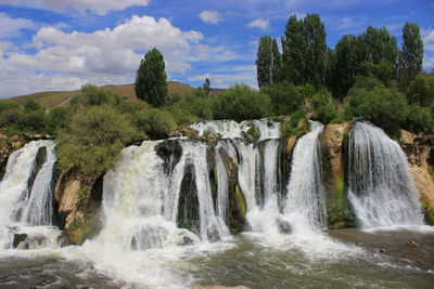 Scenic view of waterfall in forest against sky