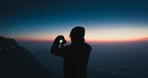 Silhouette man photographing camera against sky during sunset