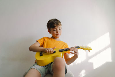 Cute boy learns to play the yellow ukulele guitar in home. cozy home.
