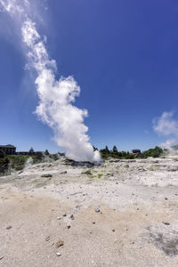 Smoke emitting from volcanic landscape against blue sky