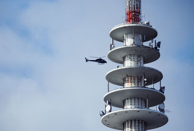 Low angle view of helicopter flying by air traffic control tower by sky