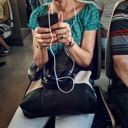 Midsection of woman listening music while sitting on chair