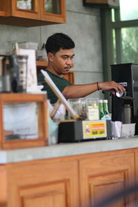 A man in a cooffeeshop counter, preparing a coffee