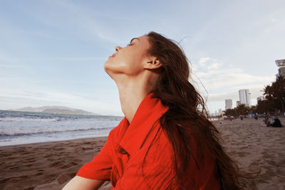 Young woman looking at beach against sky