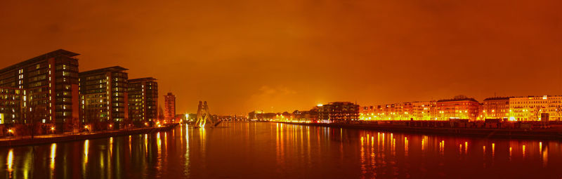 Illuminated buildings by river against sky at night