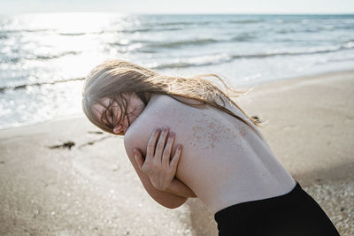 Shirtless woman hugging self at beach