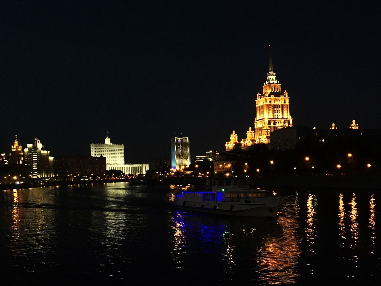 ILLUMINATED BUILDINGS BY RIVER AT NIGHT