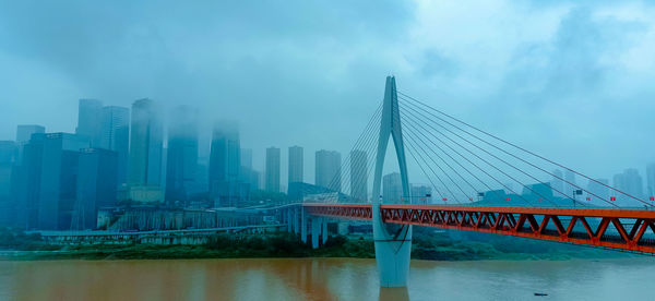 Bridge over river by buildings against sky in city