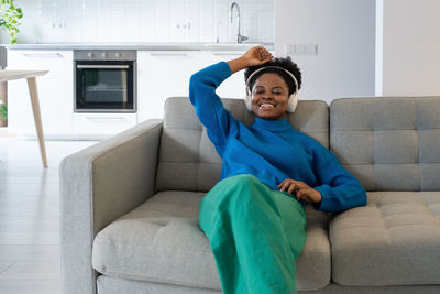 Happy relaxed african american woman in headphones closing eyes enjoying music sits on sofa