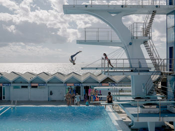 PEOPLE IN SWIMMING POOL AGAINST SKY