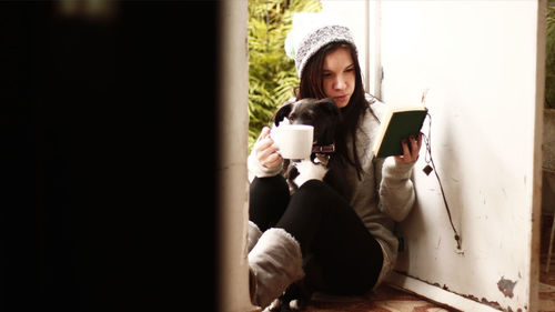 Girl reading novel while sitting with dog and coffee at doorway