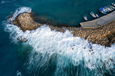 Aerial drone view of fishing boats moored at the harbor at breakwater. stormy waves at sea